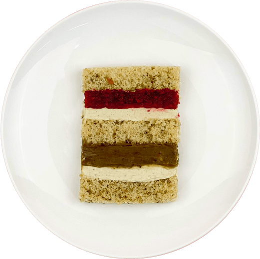 Шматочок торту з двошаровою фісташково-малиновою начинкою на тарілці.