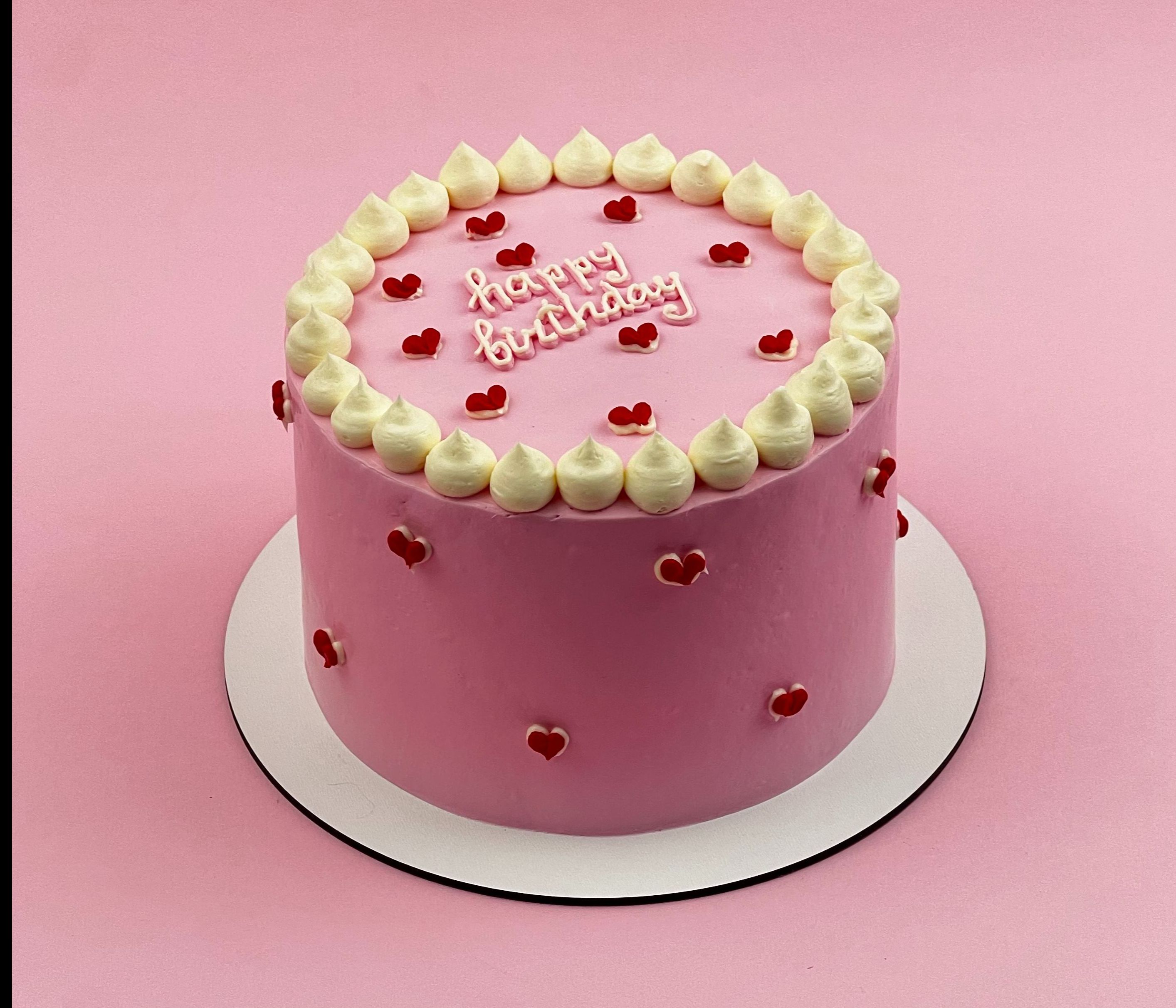 Рожевий торт середнього розміру з декоративними елементами та написом до дня народження.